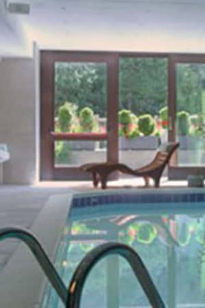 Indoor swimming pool at Hotel Cristallo with wooden panelling, folded towels, and a sun lounger by large windows.