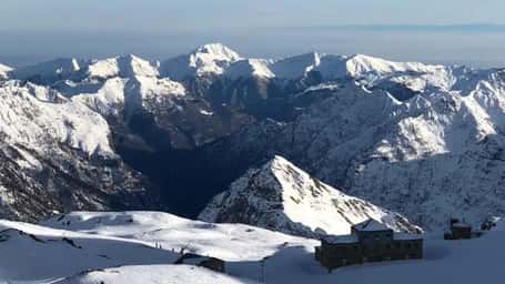 Snow-capped mountain landscape with clear blue sky, featuring prominent peaks and deep valleys, as seen from a high viewpoint.
