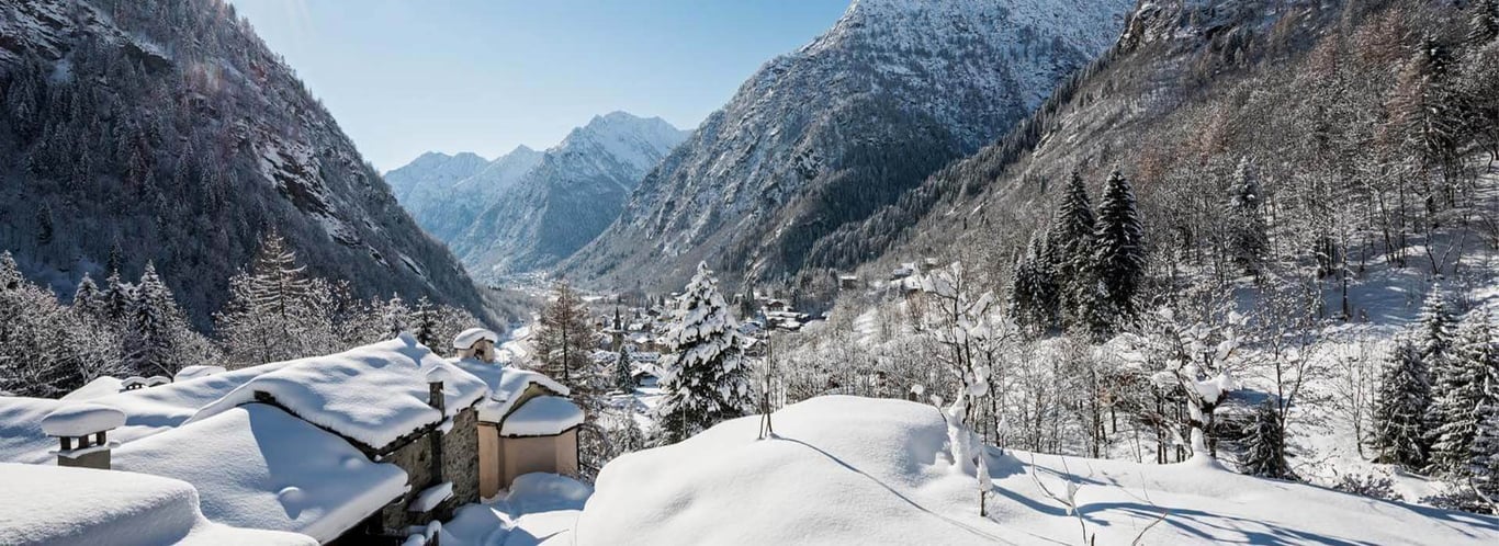 Winter view from Hotel Cristallo of snow-covered Aosta Valley mountains and rooftops under a blue sky.
