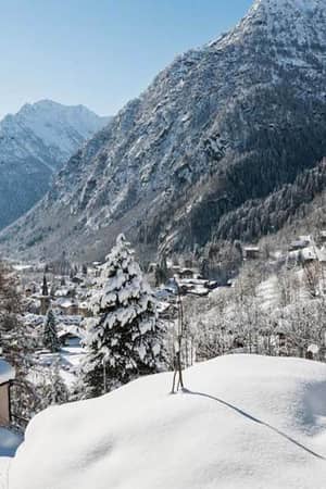 Winter view from Hotel Cristallo of snow-covered Aosta Valley mountains and rooftops under a blue sky.