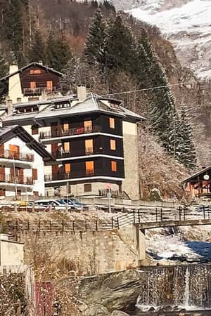 Hotel Cristallo in the Alps, surrounded by snow-laden trees, mountain peaks, and a flowing stream under a clear sky.