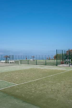 Outdoor tennis court at Hotel Impressive Playa Granada with green court surface and surrounding greenery.