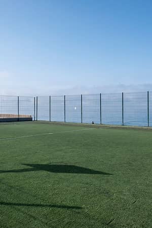Tennis court overlooking the sea at Hotel Impressive Playa Granada, with a clear sky and enclosed fencing.