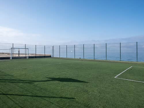 Tennis court overlooking the sea at Hotel Impressive Playa Granada, with a clear sky and enclosed fencing.