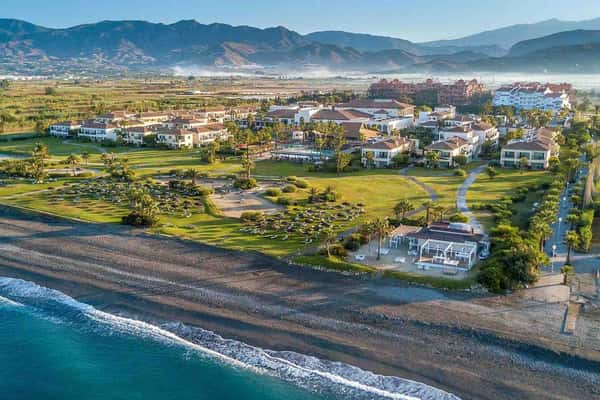 Aerial view showcasing Hotel Impressive's beachfront location, expansive lawns, sandy beach, and surrounding mountains.