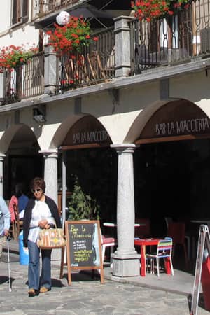 Hotel Monterosa Bar exterior with patrons dining at outdoor tables, stone arches, and red flower accents.