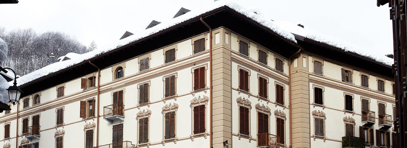 Exterior view of Hotel Monterosa, showcasing classic architecture with wooden shuttered windows and snow-covered mountain scenery.
