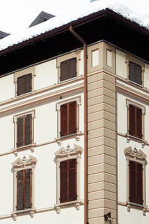 Exterior view of Hotel Monterosa, showcasing classic architecture with wooden shuttered windows and snow-covered mountain scenery.