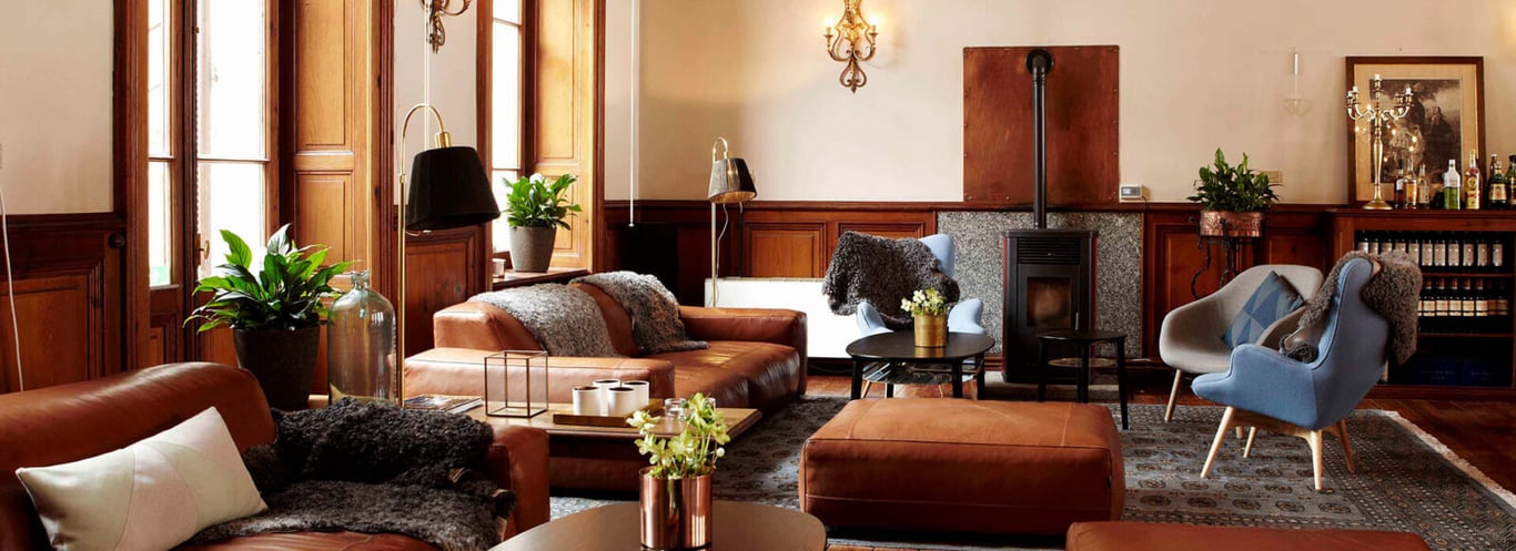 Luxurious hotel lounge with leather sofas, armchairs, plants, vintage lighting, and a bookshelf in a wood-finished interior.