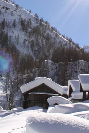 Snow-covered wooden cabins at Hotel Monterosa, surrounded by the Swiss Alps under a bright blue sky.
