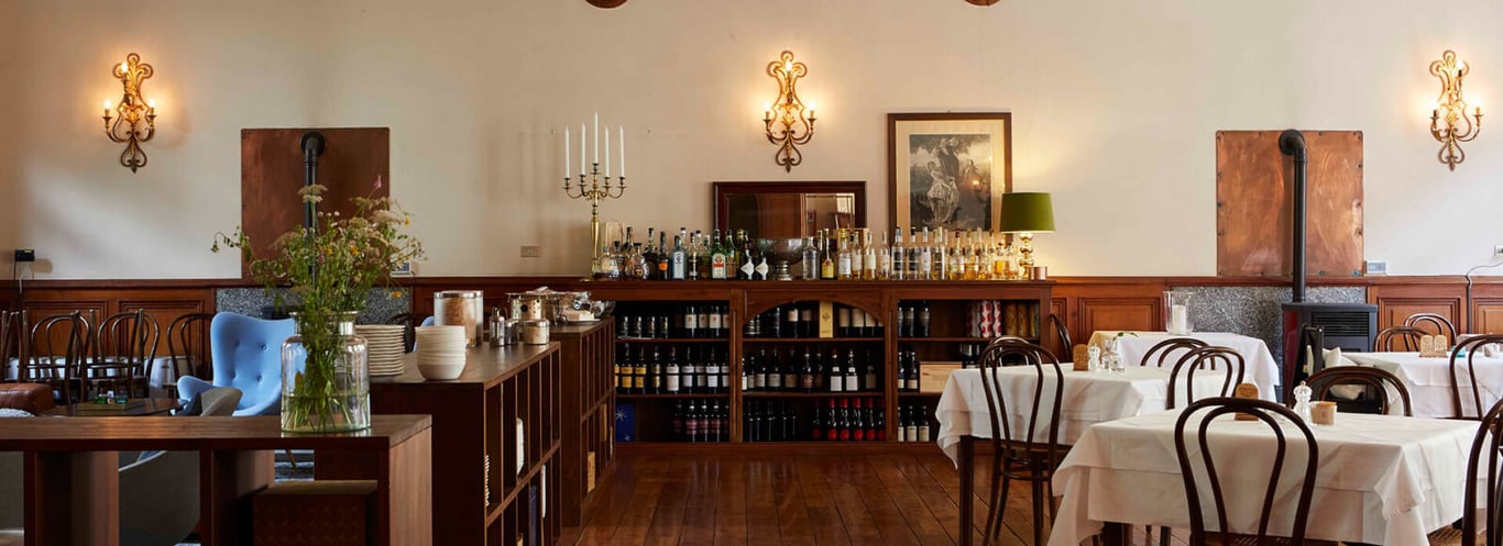 Dining room at Hotel Monterosa with white tablecloths, wooden chairs, and a display of wines and spirits, warmly lit by wall sconces.