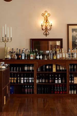 Dining room at Hotel Monterosa with white tablecloths, wooden chairs, and a display of wines and spirits, warmly lit by wall sconces.