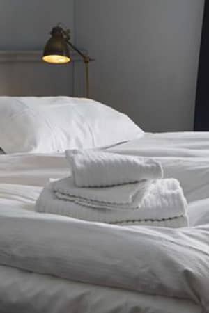 Hotel Monterosa room with a queen-sized bed covered in white linens and towels, softly lit by bedside lamps with a window in the background.