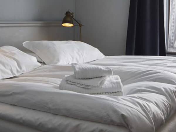 Hotel Monterosa room with a queen-sized bed covered in white linens and towels, softly lit by bedside lamps with a window in the background.