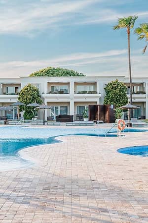 View of Hotel Vincci Costa Golf with a large swimming pool, sun loungers, palm trees, and modern hotel buildings in the background.
