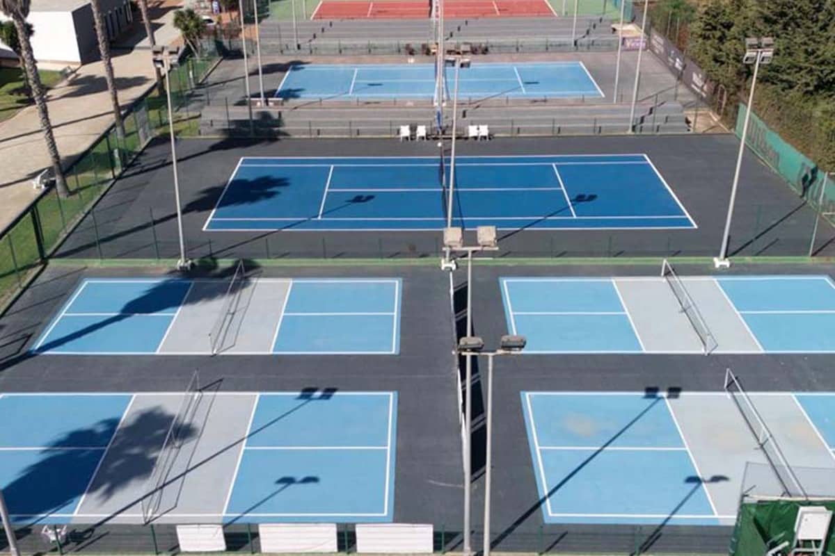 Aerial view of blue and red tennis courts at Hotel Vincci Costa Golf, surrounded by green fencing and landscaping.
