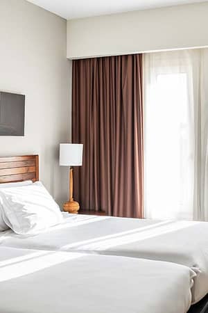 Hotel room at Vincci Costa Golf with twin beds, white bedding, wooden headboard, wicker chair, and brown curtains.