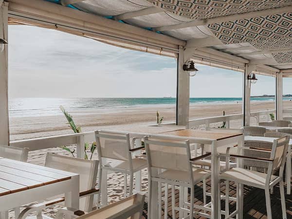 Beachfront restaurant terrace at Hotel Vincci Costa Golf with white furniture overlooking the sandy beach and ocean.
