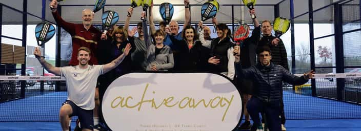 Group of people celebrating with rackets on a padel court under a tent, featuring an Active Away banner.