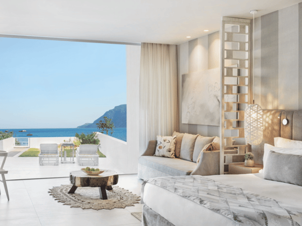Ikos Aria deluxe junior suite with private garden and sea view, featuring an open-plan room with modern decor, a double bed, seating area, and a terrace overlooking the sea.