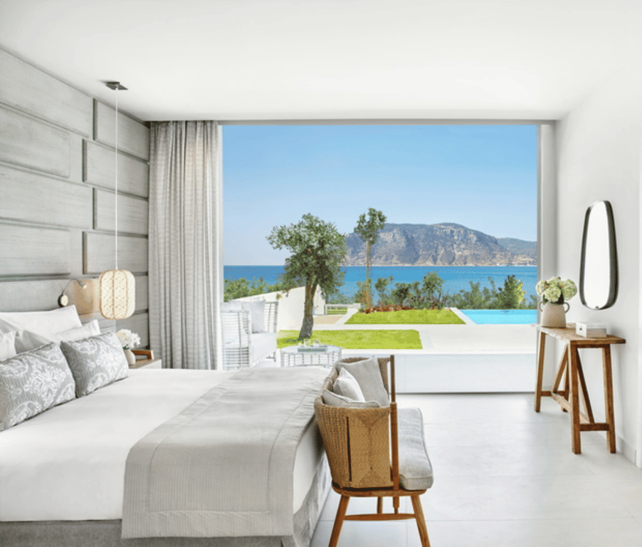 Ikos Aria suite with a private pool and sea view, featuring a bright bedroom with elegant decor, overlooking a terrace with stunning scenery.