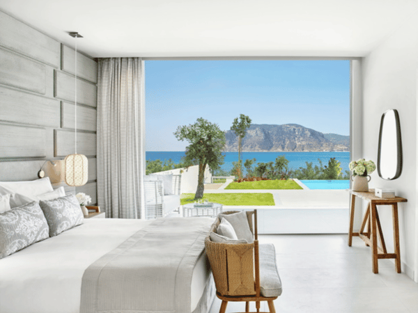 Ikos Aria suite with a private pool and sea view, featuring a bright bedroom with elegant decor, overlooking a terrace with stunning scenery.