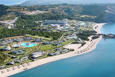 Aerial view of Ikos Aria resort, featuring multiple pools, lush gardens, accommodation facilities, and a stunning beach on a picturesque coastline.