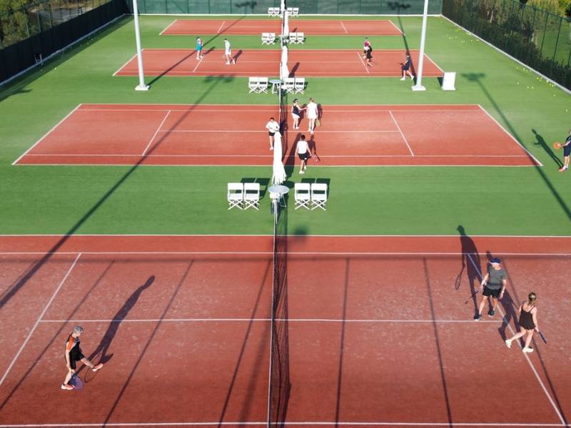 Aerial view of tennis courts at Ikos Aria resort with players on the courts enjoying tennis matches.