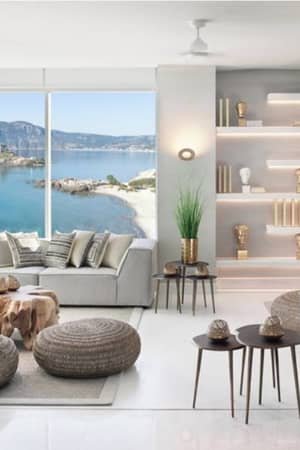 Ikos Aria hotel lobby with modern decor, neutral seating, sea view through large windows, wooden tables, and illuminated decorative shelving.