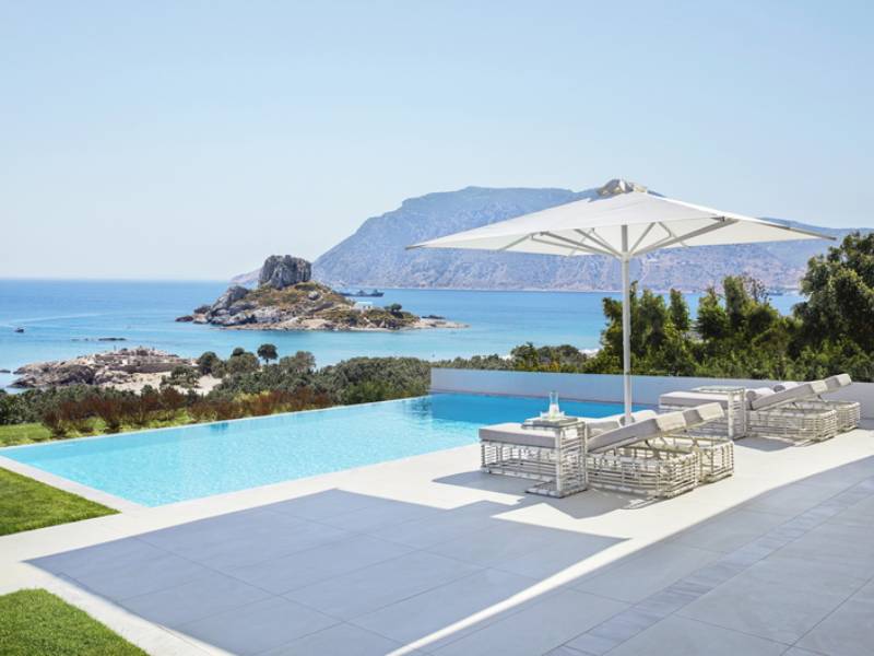 Private infinity pool at Ikos Aria with sun loungers and parasol, overlooking the Aegean Sea and mountains.