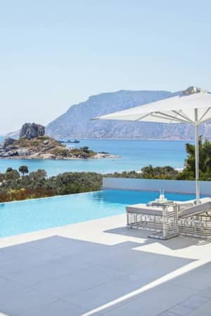 Private infinity pool at Ikos Aria with sun loungers and parasol, overlooking the Aegean Sea and mountains.