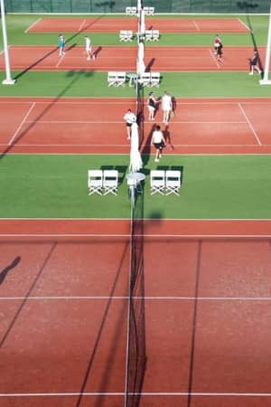 Overhead view of tennis courts at Ikos Aria with players and sunlight casting shadows, surrounded by greenery.
