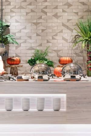 Ikos Aria dining area with a chef at a buffet table, featuring pumpkins, silver cloches, and green plants in a modern setting.