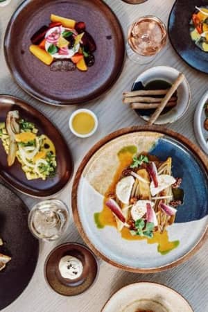 Overhead view of gourmet dishes at Ikos Aria, displaying mixed foods such as grilled fish, pasta, salads, and desserts on elegant plates.