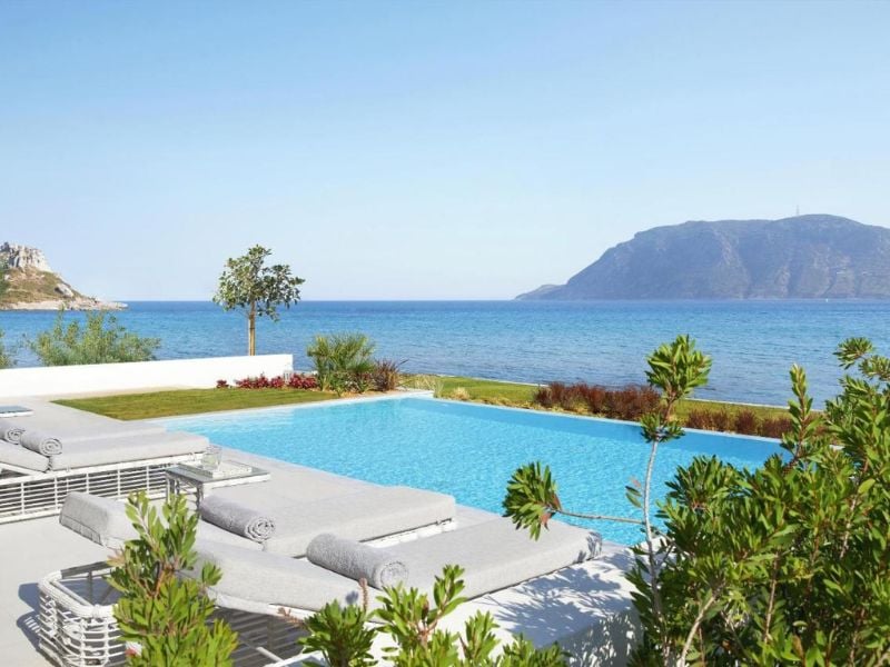 Private pool at Ikos Aria resort with sea view, sun loungers, and mountain in background.