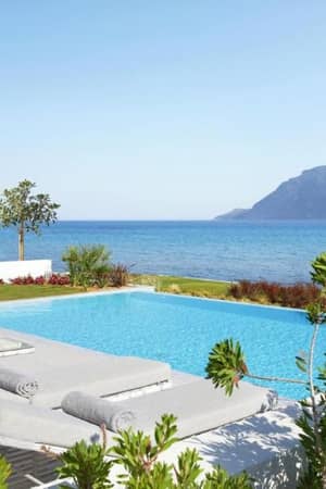 Private pool at Ikos Aria resort with sea view, sun loungers, and mountain in background.