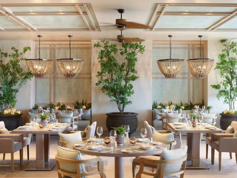 Elegant dining area at Ikos Aria with chandeliers, plants, and neatly arranged tables.