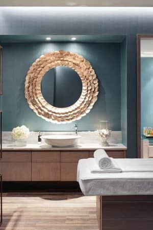 Luxurious spa treatment room at Ikos Aria with a treatment bed, circular mirror, modern decor, and ambient lighting for a serene experience.