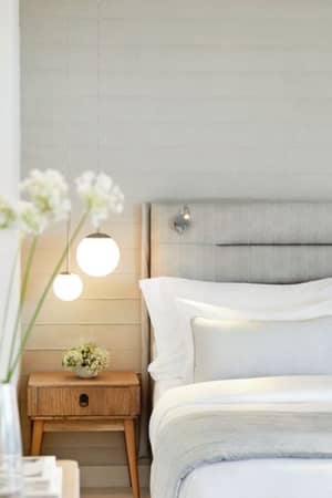 Elegant bedroom at Ikos Aria hotel with a double bed, light grey linens, a wooden nightstand, soft ambient lighting, and a mirror.