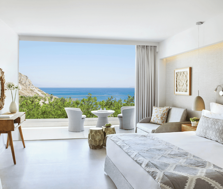 Ikos Aria Superior Room with king-size bed, private balcony, and side sea view, showcasing modern furnishings and decor.