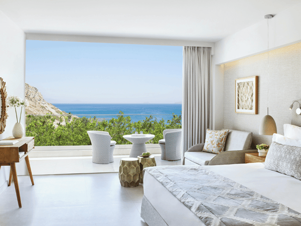 Ikos Aria Superior Room with king-size bed, private balcony, and side sea view, showcasing modern furnishings and decor.