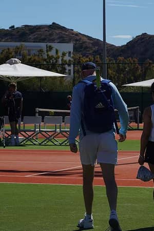 Tennis players walking towards a clay court at Ikos Aria resort with the Greek flag visible in the background.
