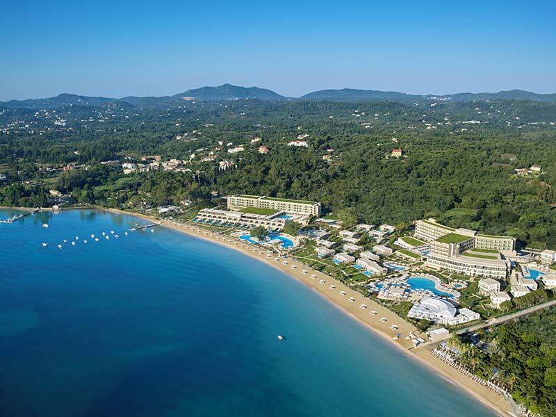 Aerial view of Ikos Dassia resort in Corfu, Greece, showcasing the resort's pools, gardens, and beach along the Ionian Sea.