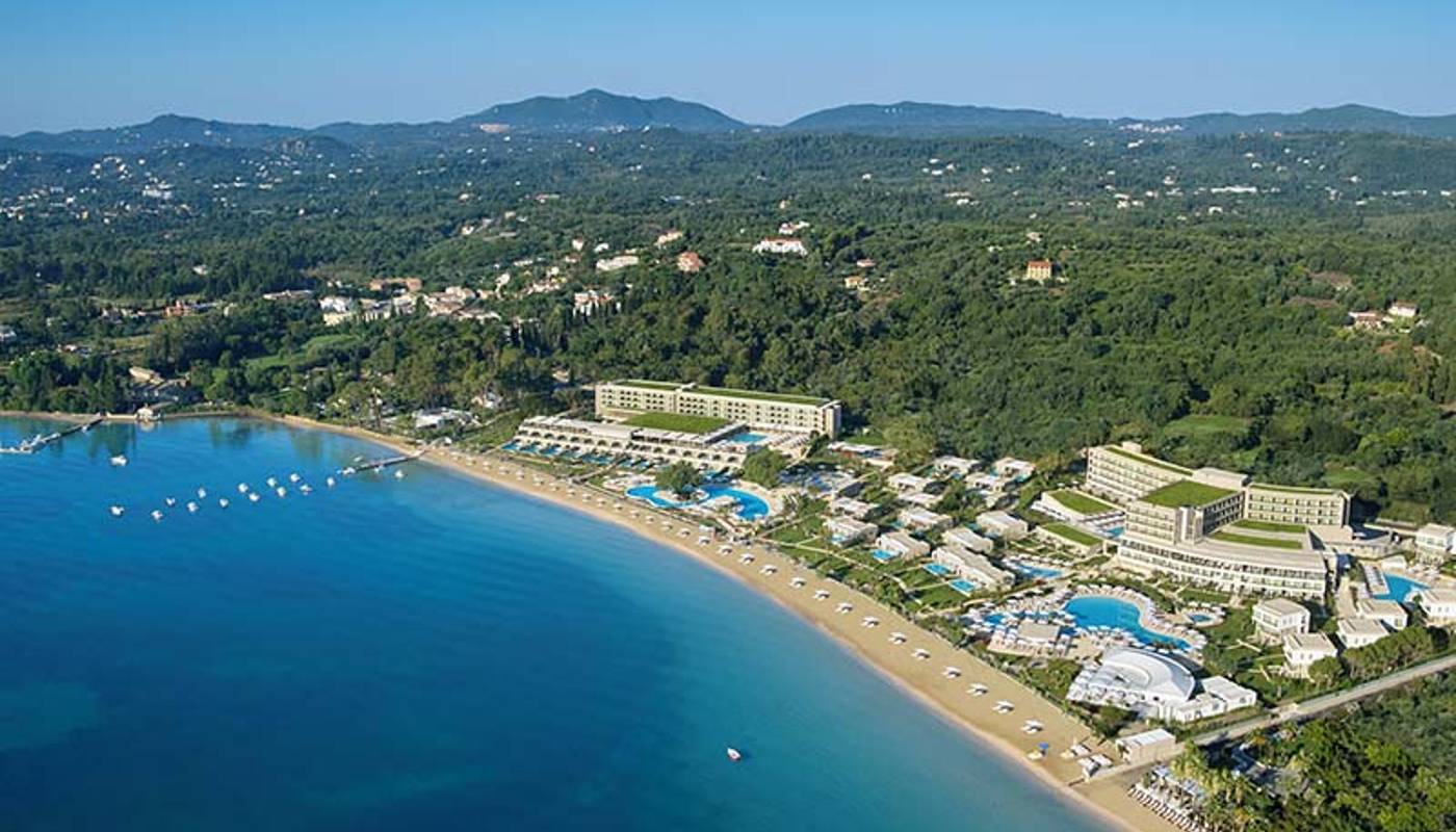 Aerial view of Ikos Dassia resort in Corfu, Greece, showcasing the resort's pools, gardens, and beach along the Ionian Sea.