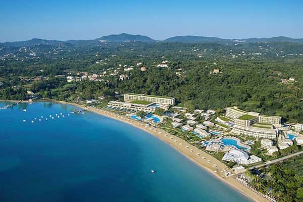 Aerial view of Ikos Dassia resort in Corfu, Greece, showcasing the resort's pools, gardens, and beach along the Ionian Sea.