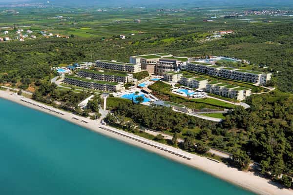 Aerial view of Ikos Oceania resort in Greece, with modern buildings, pools, beachfront, and green surroundings.