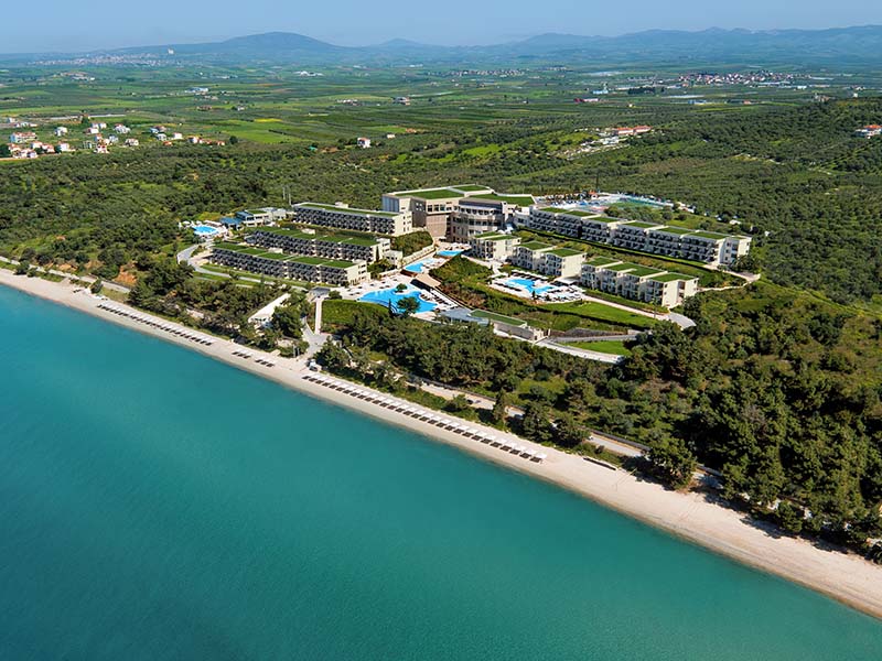 Aerial view of Ikos Oceania resort with pools, greenery, and beach access along the Aegean Sea coastline.