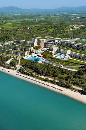 Aerial view of Ikos Oceania resort with pools, greenery, and beach access along the Aegean Sea coastline.