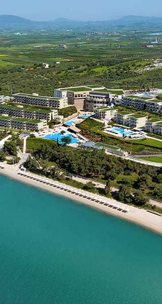 Aerial view of Ikos Oceania resort with pools, greenery, and beach access along the Aegean Sea coastline.