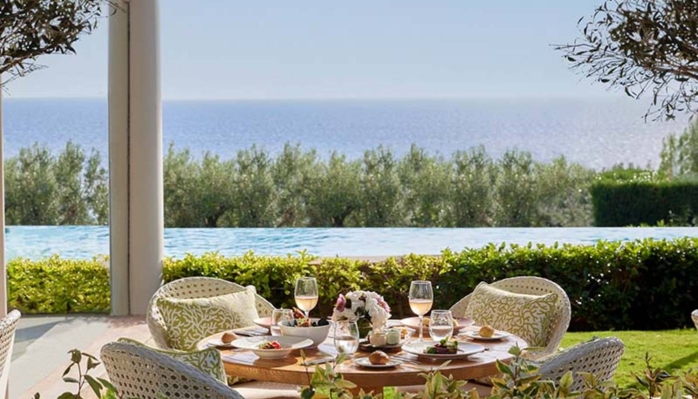 Outdoor dining area at Ikos Oceania with a table set for four, offering views of an infinity pool and the Aegean Sea.